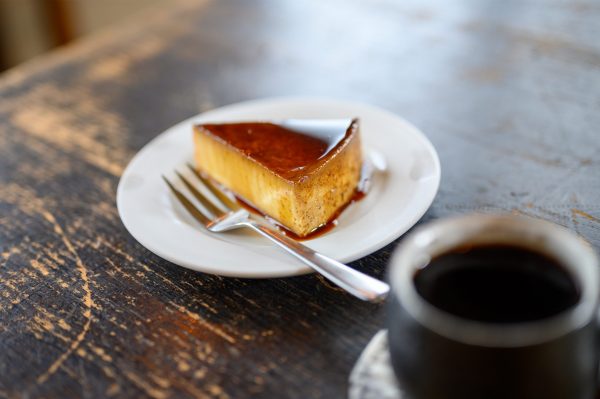 A slice of leche flan on a plate and a cup of coffee